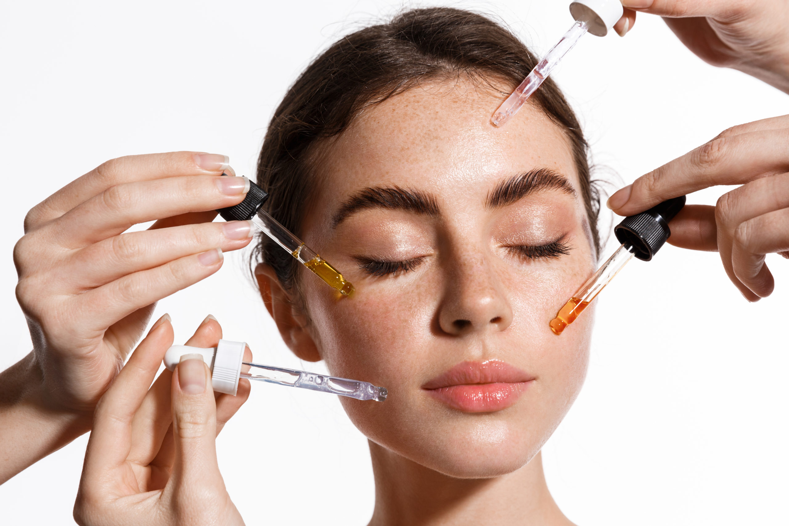 Porträt einer Frau, an deren Gesicht mehrere Pipetten mit pflegenden Seren und Hyaluron angesetzt werden – Wirkstoffkosmetik bei Donatella Beauty in Berlin Grunewald